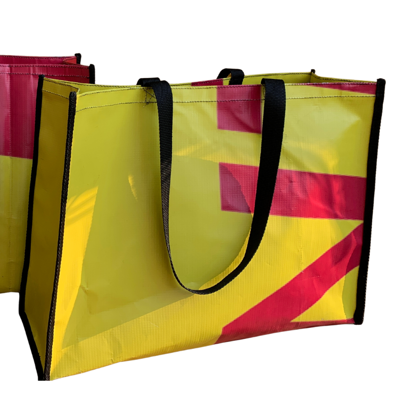 Colourful upcycled box shopper bag made from reclaimed PVC billboard banner material, standing upright with woven webbing handles
